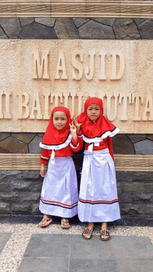 two little girls standing in front of a sign that says masjid i batu utta