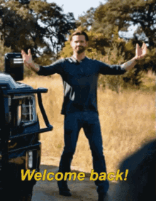 a man is standing in front of a truck with his arms outstretched and the words welcome back behind him