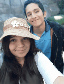 a boy and a girl are posing for a picture and the girl is wearing a hat with white flowers on it