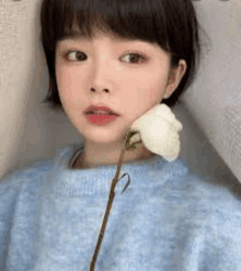 the girl is wearing a blue sweater and holding a white flower in her hand .