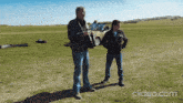 two men standing in a grassy field with a clipeo.com watermark on the bottom