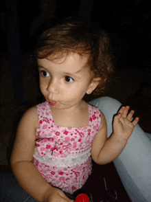 a little girl wearing a pink floral tank top holds a red lollipop