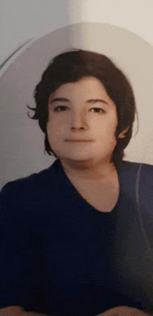 a young boy with dark hair and a blue shirt is looking at the camera