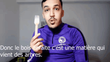 a man in a purple shirt is holding a wooden fork in his hand