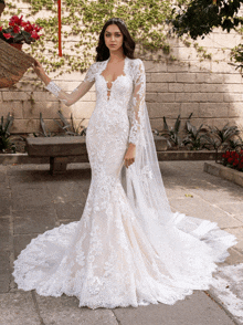 a woman in a wedding dress with long sleeves is standing in front of a brick wall