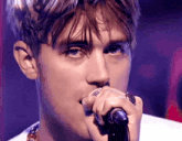 a young man is singing into a microphone with a ring on his finger