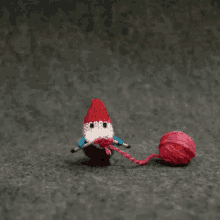 a crocheted gnome is sitting next to a ball of pink yarn .