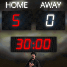 a man stands in front of a scoreboard that reads home 5-0 away 0