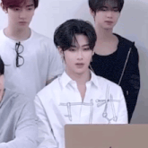 a group of young men are standing around a laptop computer . one of the men is wearing glasses .