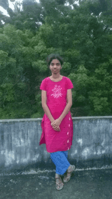 a woman in a pink top and blue pants stands on a ledge