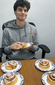 a young man is sitting at a table eating a cinnamon roll