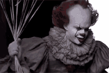 pennywise the clown from it is holding a bunch of balloons in his hand .