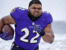 a man in a purple jersey with the number 22 on it is running with a football
