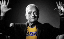 an older man wearing a lakers jersey with his hands up