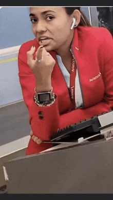 a woman in a red suit is sitting at a desk with a keyboard and lipstick on her lips .