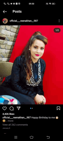 a woman is sitting in front of a red wall and a phone screen shows a post from official reenakhan 987