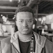 a black and white photo of a young man wearing glasses and a lanyard with a skull and the letter g on it