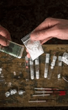 a person is holding a bag of cocaine next to a bag of money on a table .