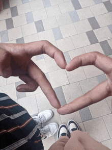 a person making a heart shape with their fingers on a tiled floor