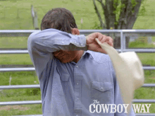 a man in a blue shirt is holding a cowboy hat with the cowboy way written on the bottom right