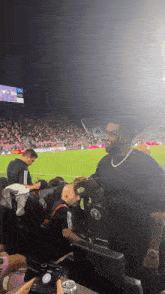 a man stands in the stands at a soccer game wearing a black shirt with the word adidas on it