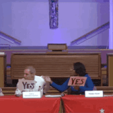 a woman holds up a sign that says yes in front of a man