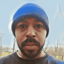 a man with a beard wearing a blue beanie looks at the camera