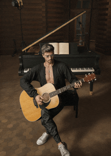 a man playing an acoustic guitar in front of a grand piano