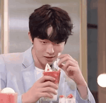 a man in a suit is eating ice cream from a red cup .