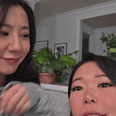 two women are sitting next to each other in a room with potted plants in the background