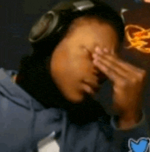 the woman is wearing headphones and covering her face with her hands .