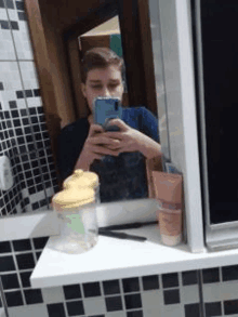 a young man is taking a selfie in a bathroom mirror with his cell phone .