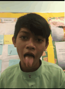 a young boy sticking his tongue out in front of a bulletin board with english written on it