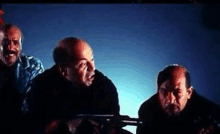 three bald men are standing next to each other in a dark room holding guns .