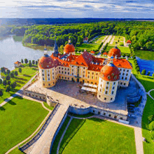 an aerial view of a large castle with a lake in the background surrounded by trees and grass .