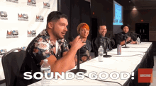 a group of people sitting at a table with bottles of water and a sign that says " sounds good "