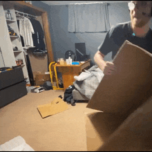 a man holding a cardboard box in a messy room with a shirt that says " i love you "