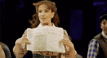 a woman is holding a newspaper in her hands that says `` newsies stop the world '' .