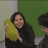 a woman is holding a green pillow and smiling at a man