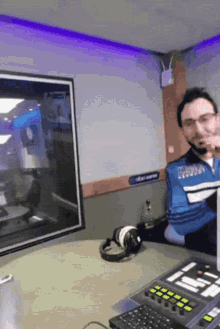 a man sitting at a desk in front of a monitor with a sign on the wall that says abc radio