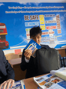 a boy holds a book in front of a sign that says be safe be honest