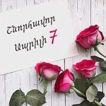 a bunch of pink roses sitting on top of a wooden table next to a sign .