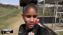 a woman in a black nike shirt is standing in front of a fence with minas do timao written on it