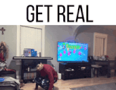 a man is squatting down in front of a television with the words get real written above him