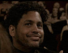 a man with curly hair is smiling in a crowd