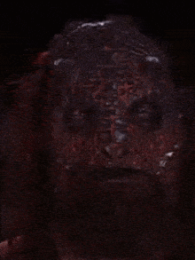 a close up of a demon 's face with horns and a beard in a dark room .