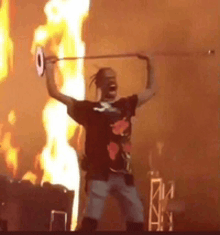 a man in a black shirt is holding a barbell over his head in front of flames