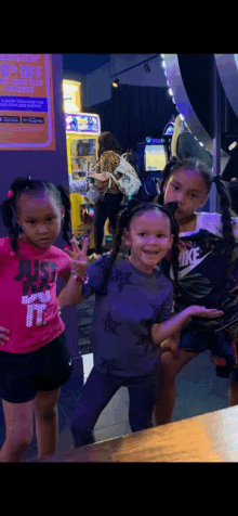 three little girls are posing for a picture in an arcade . one of the girls is wearing a nike shirt .