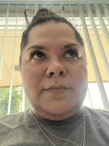 a woman wearing a gray shirt and a silver necklace looks up at the camera