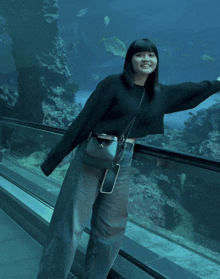 a woman in a black sweater stands in front of a large aquarium